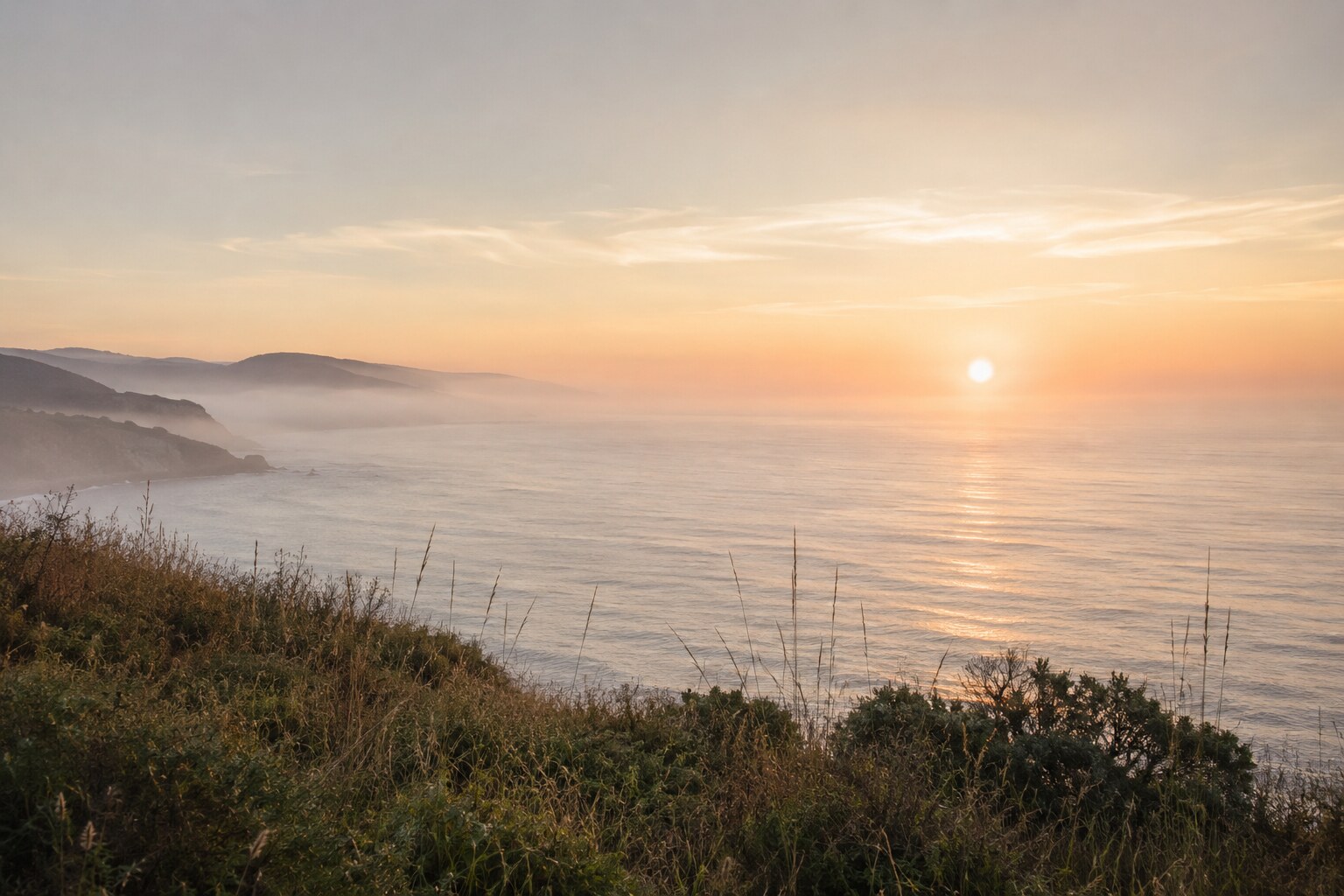 A soft sunrise over the Northern California coast, with misty headlands and native grasses.